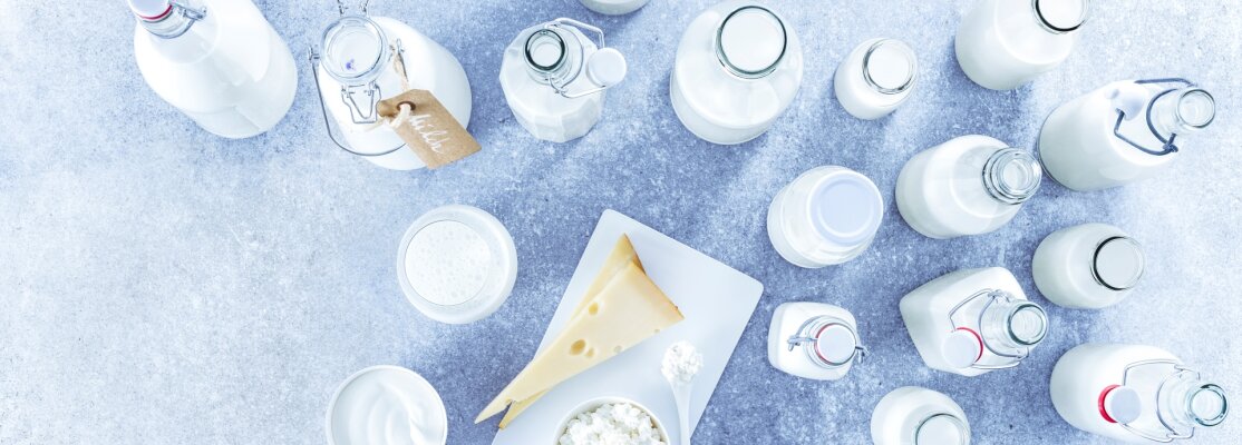Milchflaschen, Käse und Frischkäse stehen auf einer weißen Marmorplatte.
